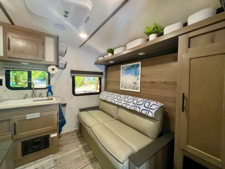 Bright RV rental interior features compact kitchen with sink, comfortable sofa, and decor shelf.. Gulf Stream Amerilite 2022