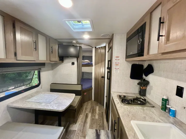 Inside this modern RV rental: a compact kitchen, dinette, and bunk beds, ready for your next road trip.. Gulf Stream Amerilite 2022
