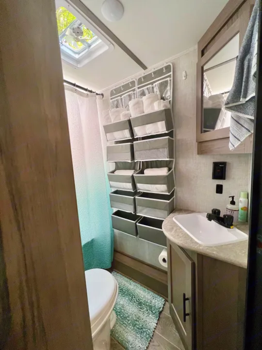 Explore this efficient RV rental bathroom, featuring a toilet, sink, shower, and smart over-door storage for supplies.. Gulf Stream Amerilite 2022