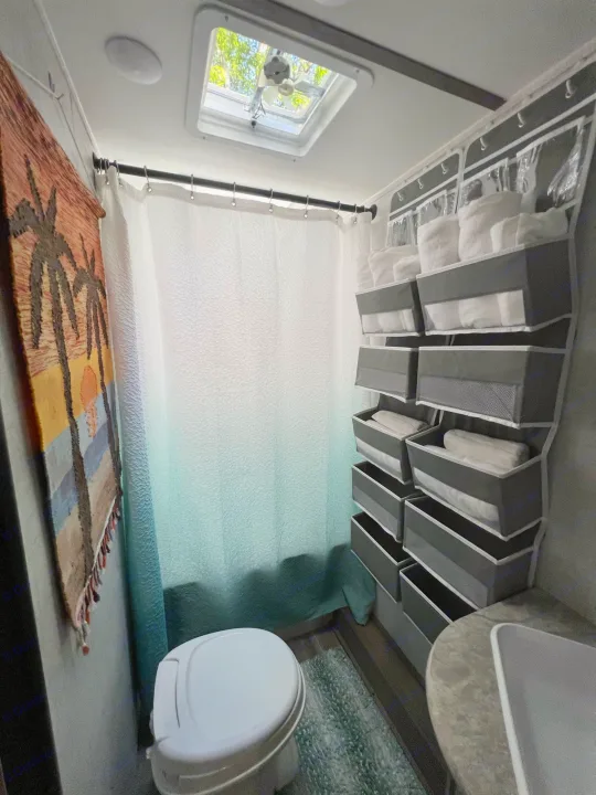 This RV rental features a practical bathroom with shower, toilet, skylight, and clever hanging storage.. Gulf Stream Amerilite 2022