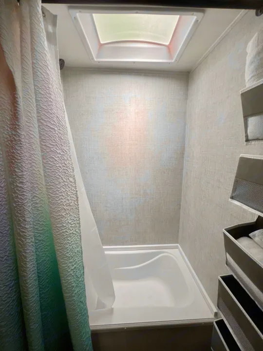 Compact RV rental bathroom featuring a bathtub, shower, skylight, and wall-mounted storage.. Gulf Stream Amerilite 2022