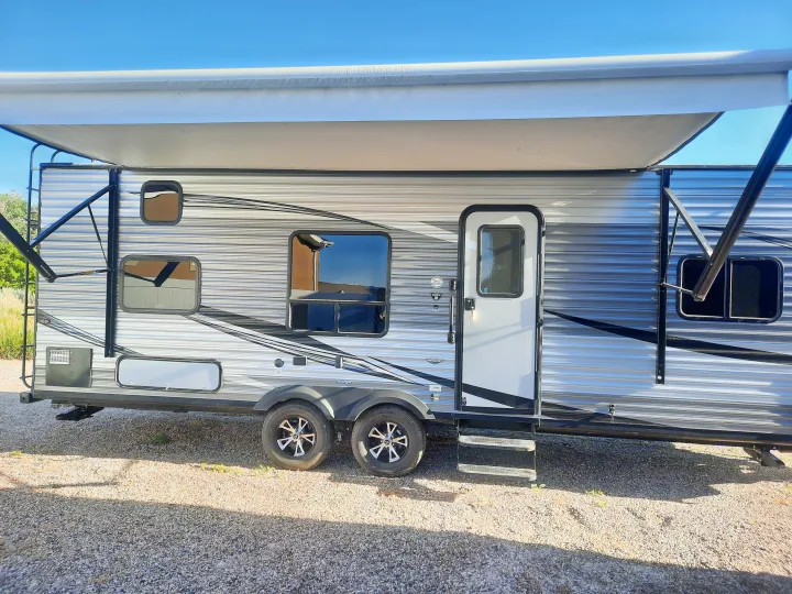 Side view of a modern silver and grey travel trailer RV rental, featuring an extended awning, windows, door, and dual axles, ready for adventure.. Jayco Jay Flight SLX 2019