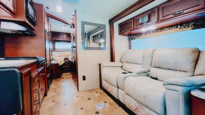 Explore this inviting rv rental interior, featuring a full kitchen, plush reclining sofa, and a private bedroom area.. Thor Vegas 2014