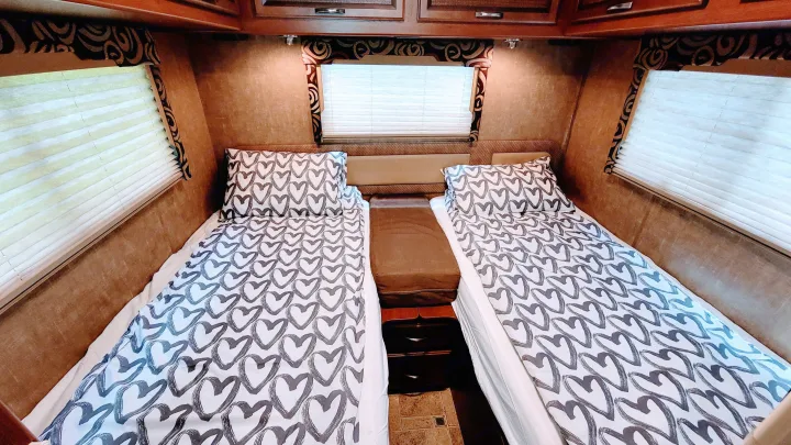 Inside an RV rental: two neatly made beds with playful heart-patterned bedding, flanked by windows & wood cabinets.. Thor Vegas 2014