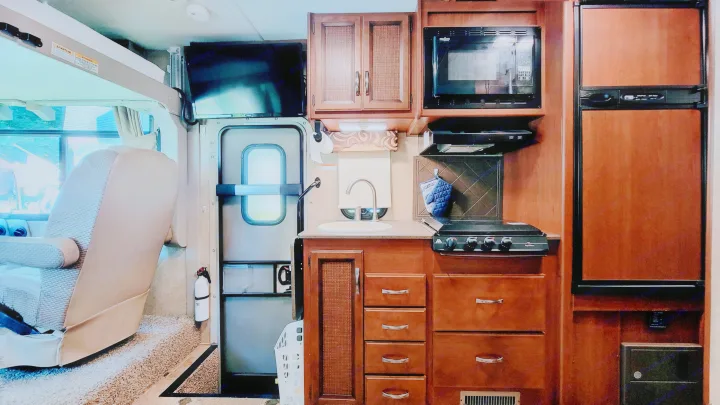 Functional RV rental interior: a compact kitchen with sink, stove, microwave, fridge, TV, and main entrance door.. Thor Vegas 2014