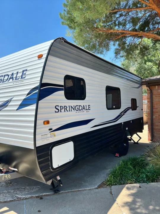 This white and blue Springdale by Keystone Mini travel trailer, a great RV rental option, is parked for your next adventure.. Keystone Springdale 2022