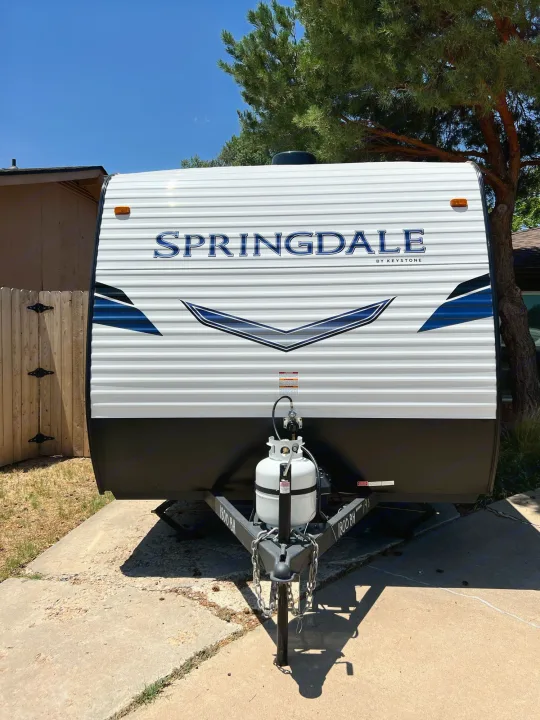 Front view of a white Springdale travel trailer RV rental, with propane tanks, parked on concrete.. Keystone Springdale 2022