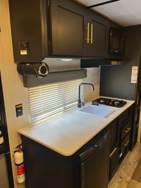 Inside a modern RV rental: compact kitchen with sink, stovetop, microwave, and overhead cabinets for convenient mobile adventures.. Keystone Springdale 2022