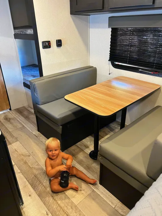 Toddler with lantern plays on wood floor inside an RV rental, featuring a dinette and bunk beds.. Keystone Springdale 2022