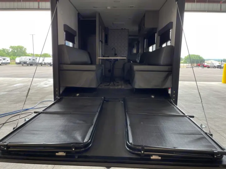 RV rental interior: A toy hauler's rear ramp is down, showing two fold-out beds and an internal living area with sofas.. Coleman 270TQ 2022