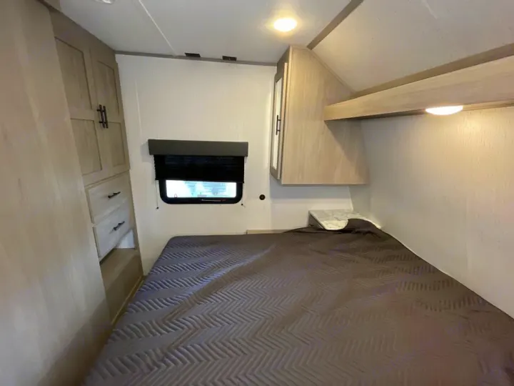 RV rental bedroom with a comfy bed, window, built-in wardrobe, and overhead storage. Compact interior for travel.. Coleman 270TQ 2022