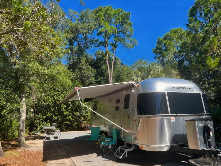Sunny day at a lush Airstream RV rental campsite. Awning extended, chairs out - ready for a relaxing outdoor adventure.. Airstream Flying Cloud 25RB 2022
