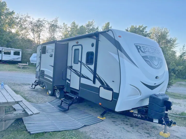 A Rezerv travel trailer RV rental, with an extended slide-out and awning, is parked at a campground with a picnic table.. Crossroads RV Rezerve 2016