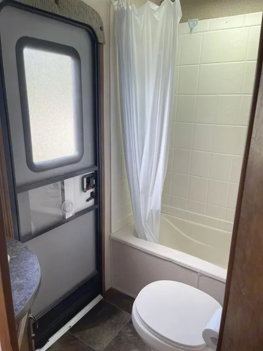 RV rental bathroom featuring a toilet, tub/shower with curtain, and RV entry door. A compact, functional space.. Crossroads RV Rezerve 2016