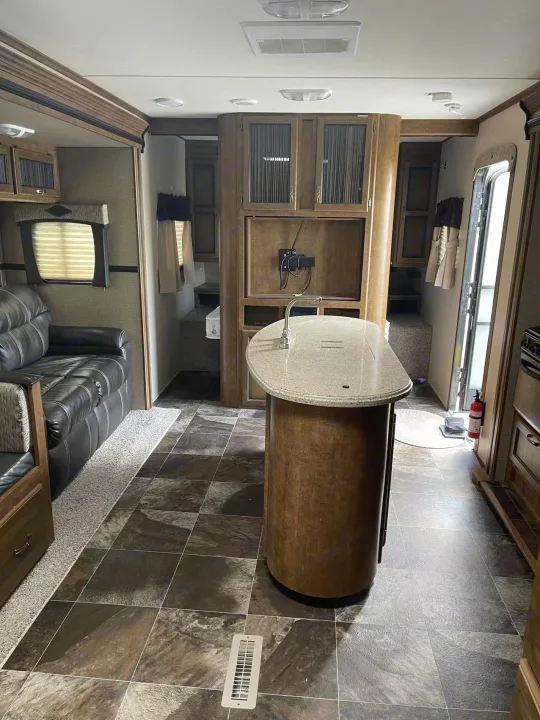 Spacious RV rental interior featuring a modern kitchen island, living area with sofa, and tiled flooring. Ideal for comfortable travel.. Crossroads RV Rezerve 2016