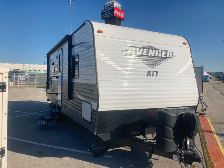 Avenger ATI RV rental by Prime Time Mfg. parked at Kansas Speedway, with stadium seating and sponsor signs visible.. Avenger ATI 2018