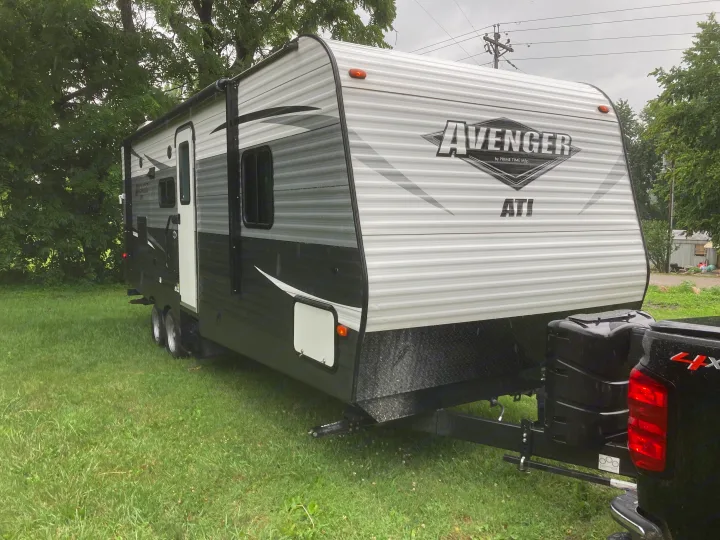 This black and white Avenger travel trailer RV rental is parked on green grass, ready for your next adventure.. Avenger ATI 2018
