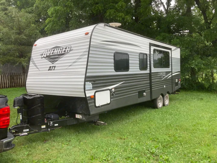 Avenger AT1 travel trailer rv rental hooked to a black truck, parked on green grass with trees in the background.. Avenger ATI 2018