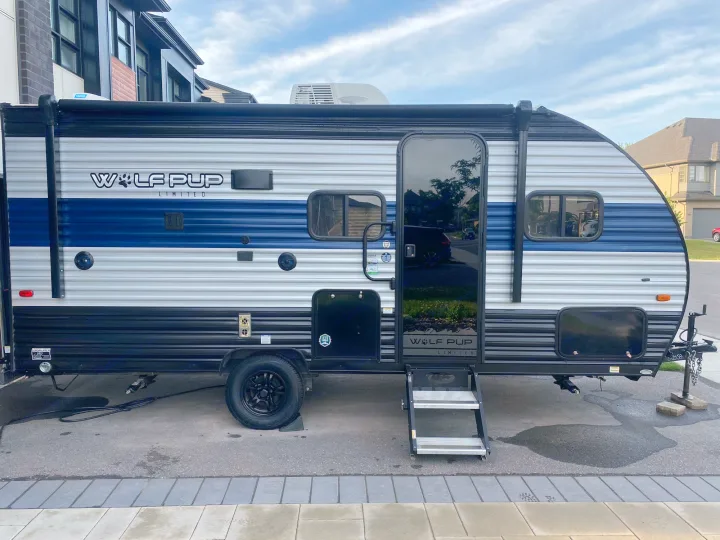 A blue and white Wolf Pup Limited travel trailer, an excellent RV rental. The camper is parked on pavement with steps out.. Forest River Wolf Pup 2021