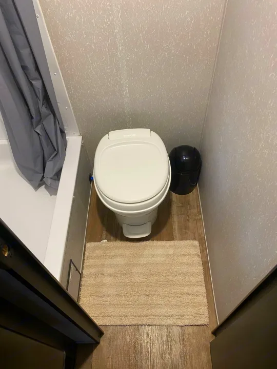 Functional RV rental bathroom: compact white toilet, gray shower, and black bin on wood floor.. Forest River Wolf Pup 2021
