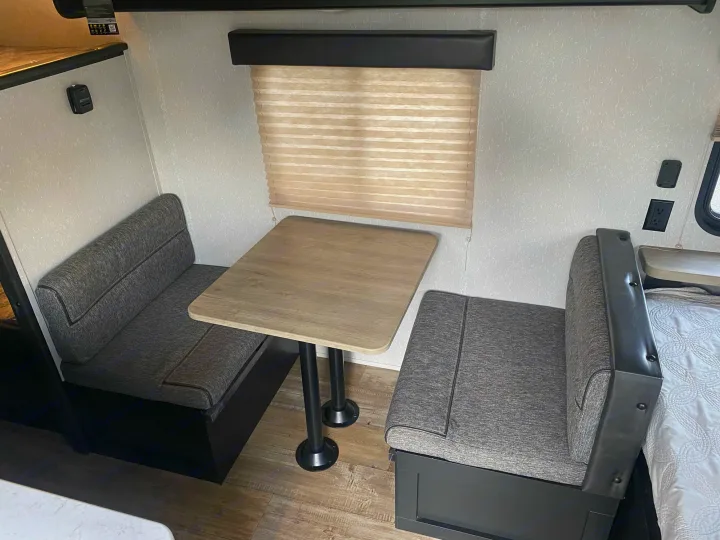 This RV rental features a cozy dinette area with gray upholstered benches and a light wood-grain table. Perfect for meals in your camper.. Forest River Wolf Pup 2021