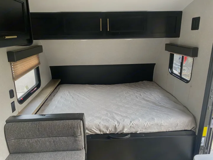 Cozy RV rental bedroom with patterned bed, black cabinets, and side windows. Ideal for travel trailer stays.. Forest River Wolf Pup 2021