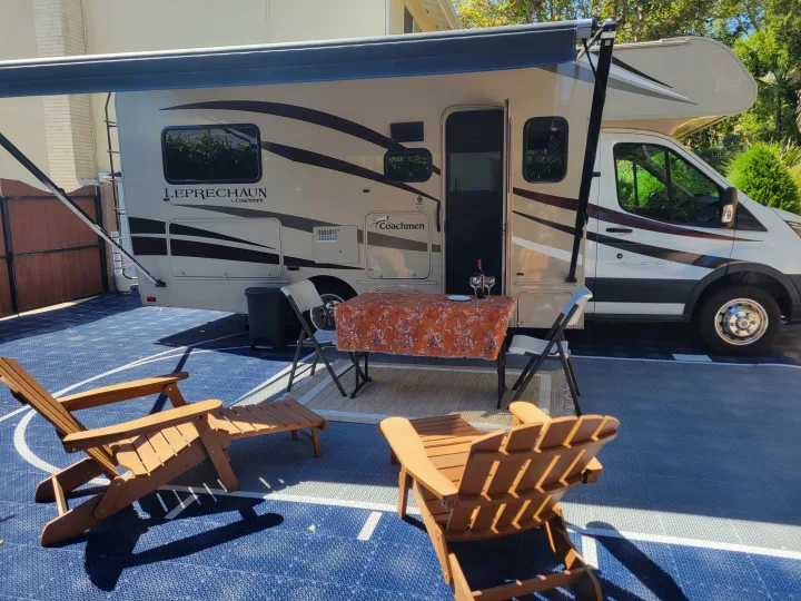 An RV rental (Coachmen Leprechaun) set up for outdoor relaxation with a table, wine, and chairs on a blue tiled patio.. Coachman Leprechaun 2018