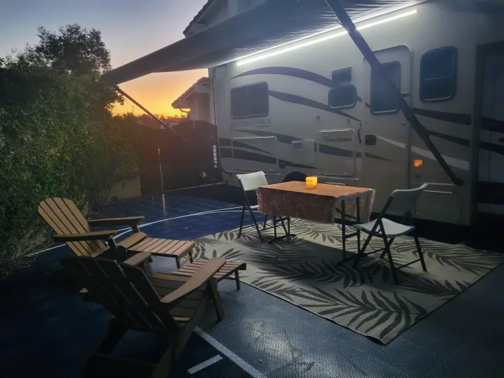 RV rental with lighted awning, outdoor patio furniture, and a dog on a dark court at sunset. Peaceful evening.. Coachman Leprechaun 2018