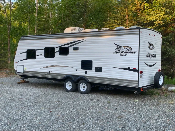 Jayco RV travel trailer, perfect for an rv rental, parked on a gravel lot in a serene wooded area.. Jayco Jay Flight 2017