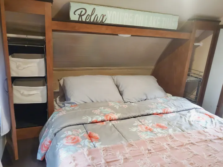 RV rental: A cozy bedroom with floral comforter, grey pillows, built-in storage, and a "Relax" sign above the bed.. Forest River Wildwood X-Lite 2017