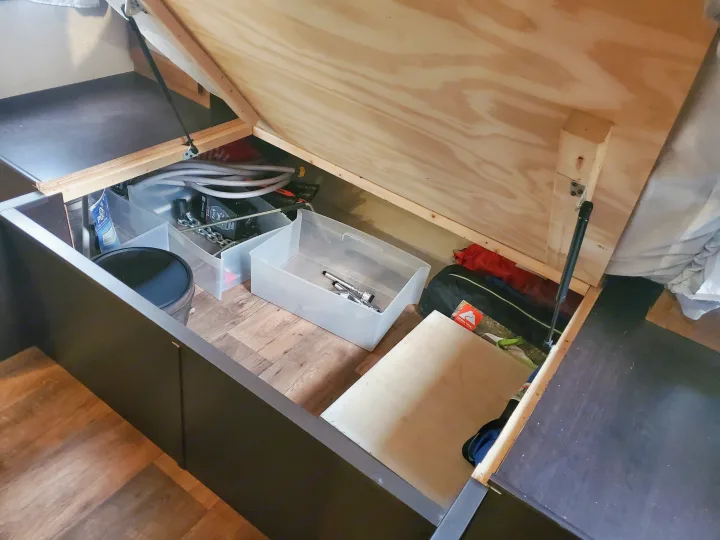 RV rental under-bed storage, showing an organized space for camping gear and other items with a lifted wooden panel.. Forest River Wildwood X-Lite 2017