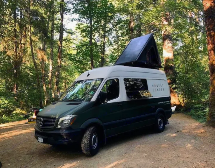 Green & white Mercedes campervan with pop-top tent, "Honest Camper," in forest. Your next RV rental adventure awaits!. Mercedes-Benz Sprinter 2017