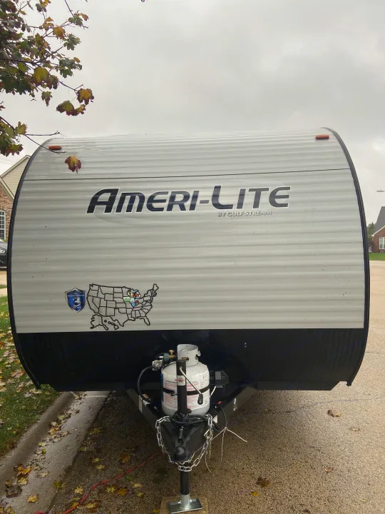 Front of a grey Ameri-Lite travel trailer, ideal for RV rental, with propane tanks and a USA map sticker visible.. Gulf Stream Ameri-Lite Super Lite 2021
