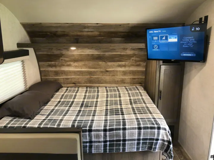Cozy RV rental bedroom featuring a comfy bed with plaid blanket, wood-paneled wall, and smart TV for entertainment.. Gulf Stream Ameri-Lite Super Lite 2021