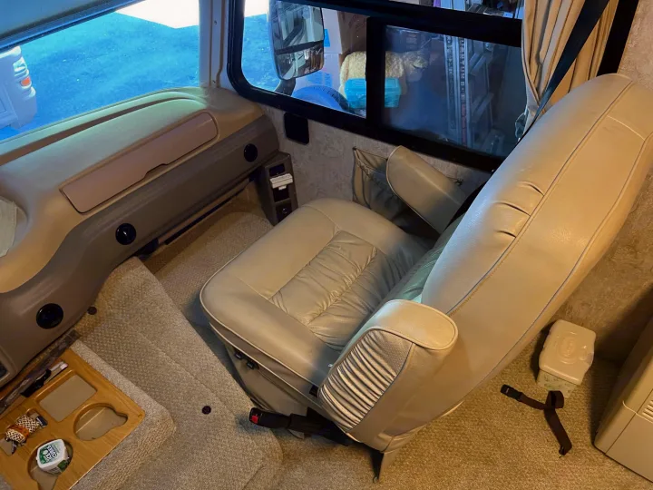 Inside a clean rv rental, featuring the comfortable captain's chair, dashboard, and window. Floor items include a tray & wipes.. National RV Sea Breeze 2006