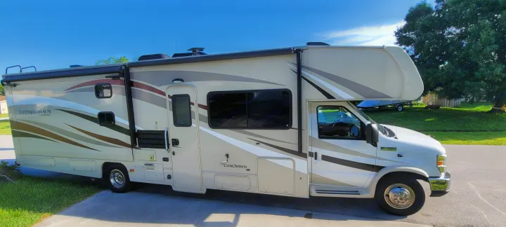 This Coachmen Leprechaun Class C RV could be your next RV rental. Shows the parked side of a beige RV with stripe graphics.. Coachmen Leprechaun 2017