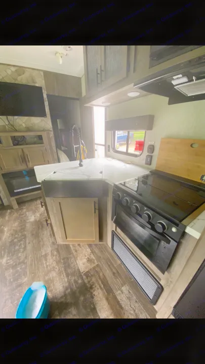 An RV rental interior showcasing a modern kitchen with stove, sink, and microwave, plus a living area with TV and fireplace.. Forest River Cherokee Wolf Pack Toy Hauler 2020
