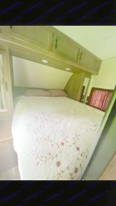Cozy RV rental bedroom with a white floral quilted bed, two pink pillows, and built-in wooden storage cabinets.. Forest River Cherokee Wolf Pack Toy Hauler 2020