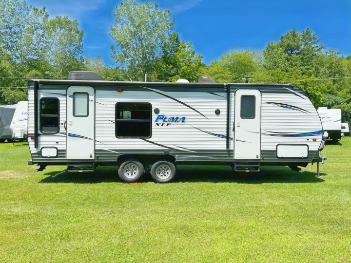 White and black Puma XLE travel trailer parked on green grass under a clear blue sky. Ideal for your next RV rental adventure.. Palomino Puma XLE 25 2018
