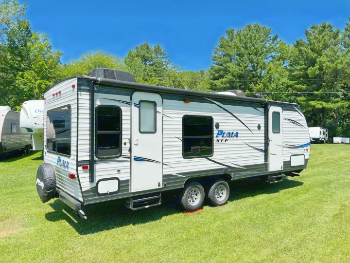 A sleek white and black Puma XLE travel trailer parked on lush green grass under a clear sky, ready for your next RV rental.. Palomino Puma XLE 25 2018