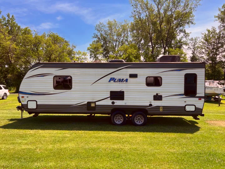 This Puma travel trailer RV rental is parked on green grass, ready for camping trips with blue sky and trees in background.. Palomino Puma XLE 25 2018