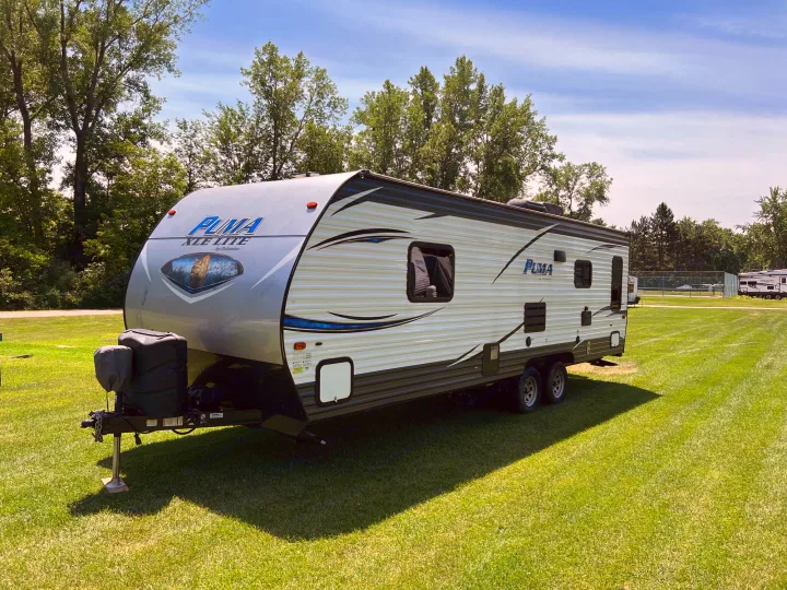 Light-colored travel trailer, a great RV rental option, parked on lush green grass beneath a clear blue sky.. Palomino Puma XLE 25 2018