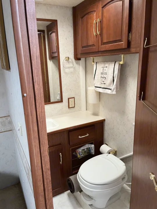 Clean and functional RV rental bathroom featuring a toilet, sink, vanity, and mirror with wood accents.. Itasca Sundancer 2001