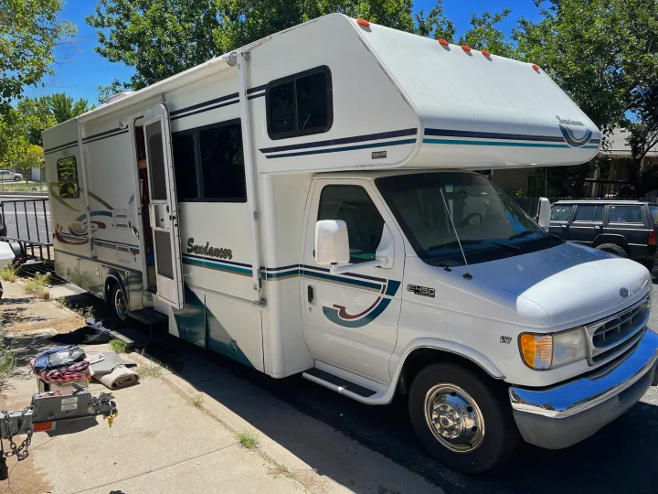 Bright white RV, a Ford E450 Super Duty motorhome with "Sundancer" decals, parked outdoors on a sunny day. Ideal for an rv rental.. Itasca Sundancer 2001