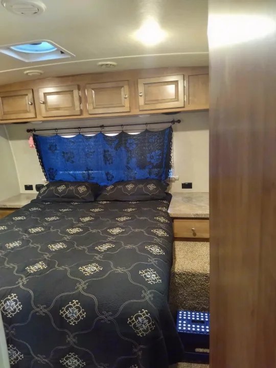 Cozy RV rental bedroom features a dark patterned bed, ample storage cabinets, and blue window fabric.. Forest River Rockwood Ultra Lite 2018