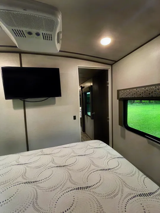 Cozy RV rental bedroom featuring a mounted TV, AC, comfortable bed, and a scenic window view of green landscape.. Forest River Salem Hemisphere 2020