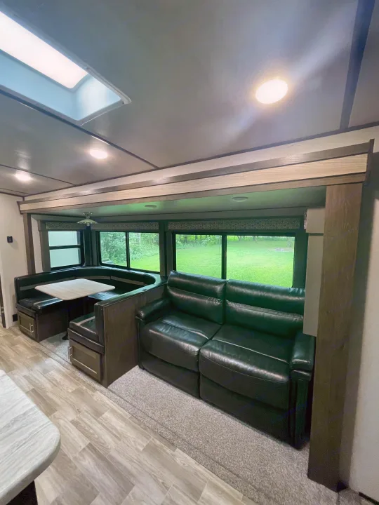 A bright RV rental interior: features a comfy black sofa, U-shaped dinette, and large windows with outdoor views.. Forest River Salem Hemisphere 2020