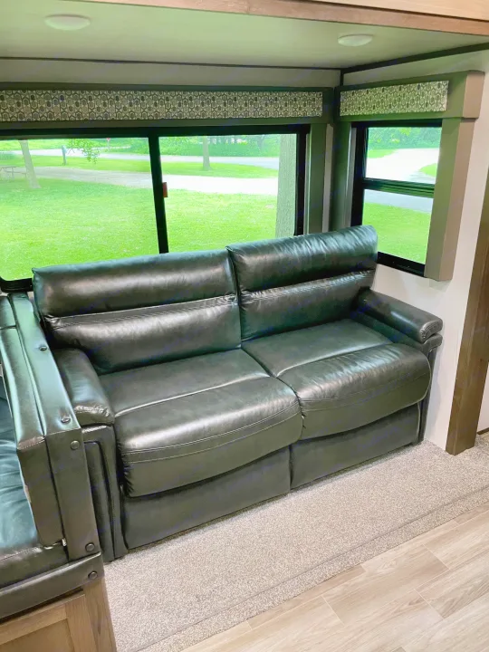 Inside an RV rental, a comfy black leather recliner sofa offers a window view of green grass and trees.. Forest River Salem Hemisphere 2020