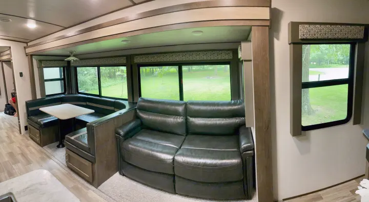 Spacious RV rental interior featuring a dining booth, comfortable leather couch, and large windows with a view of nature.. Forest River Salem Hemisphere 2020