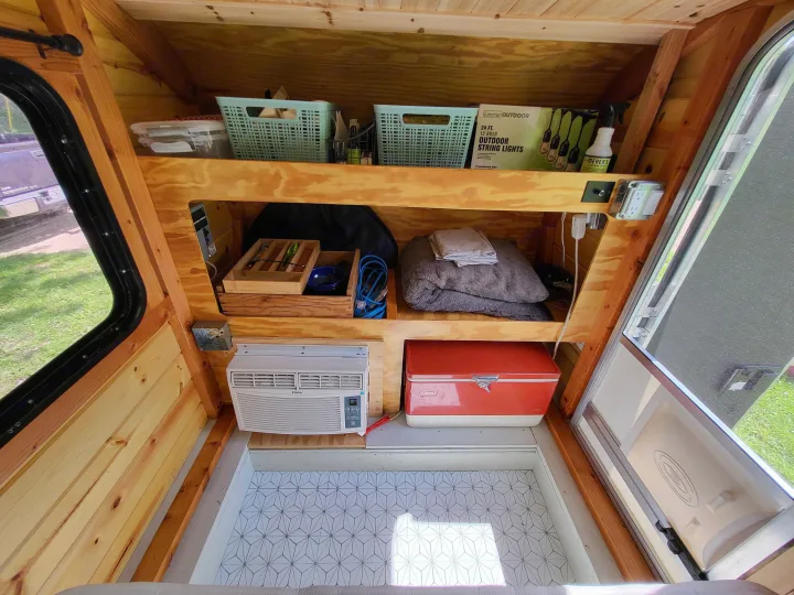 Compact rv rental interior: custom wooden shelving holds essentials, with a Haier AC unit and a red Coleman cooler for organized travels.. Custom Camper 2020